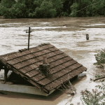 Natural hazards -a photo of flooding with only the roof of a house visible. Photo by Visual Intermezzo-sourced from Canva